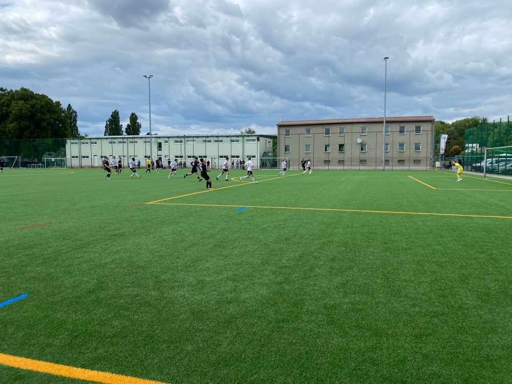 Fußballspiel auf einem Kunstrasenplatz, Gebäude im Hintergrund