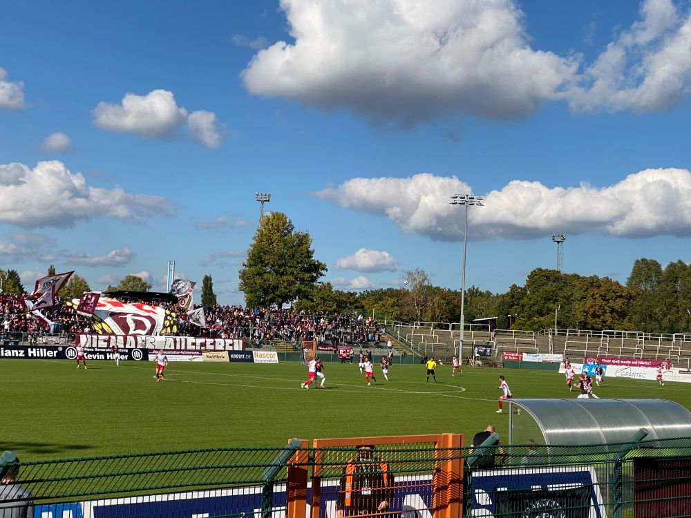 Fanblock des BFC Dynamo mit einer Blockfahne, im Vordergrund das Spielfeld 