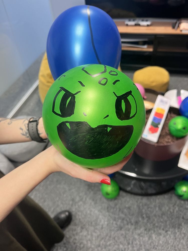 A green balloon with a bulbasaur’s face drawn on it. There is a blue balloon glued to it, imitating bulbasaur’s bulb. 