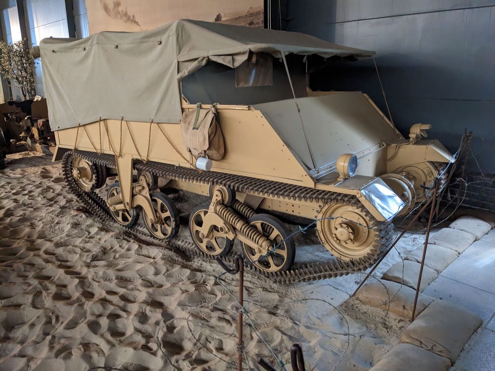A Loyd Carrier in the dark confines of the Land Warfare Hall at IWM Duxford. It's painted yellow and has a canvas roof. Holes in the vehicle frame show where the armour plates could be attached. 