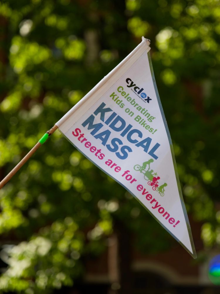 Triangular pennant flag with text
'Cyclox/ Celebrating Kids on Bikes/ KIDICAL MASS/ Streets are for everyone!' with a graphic of a cargo bike, a balance bike and a pedal bike. (credit Roger Close).