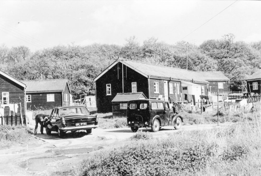 1966 black and white archive image of huts set in woodland with vehicles nearby.  (Oxfordshire History Centre, used with permission)