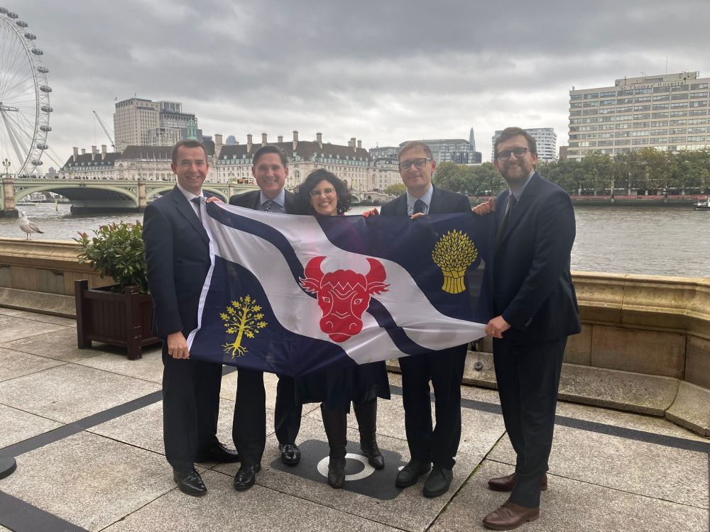the five Lib Dem MPs stand behind a flag of Oxfordshire on the balcony of the place of Westminster. The Thames and the London Eye are in the background