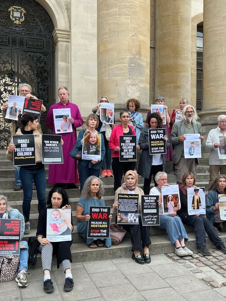 Bishop of Oxford, in purple robes, stands on steps with protesters holding placards. (via UK Friends of Standing Together) https://www.facebook.com/UKFOST/posts/pfbid0k76RJrrQQBNdrs8c39M9GiocWeZyLVeAcS5epzspoci4FFQybNt1oNRiRXSxRAJEl
