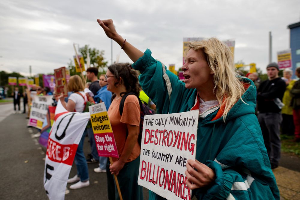 Pro immigration protesters. Blonde woman fist in air holds a sign ‘ the only minority destroying this country are billionaires’  📷 Roger Close
