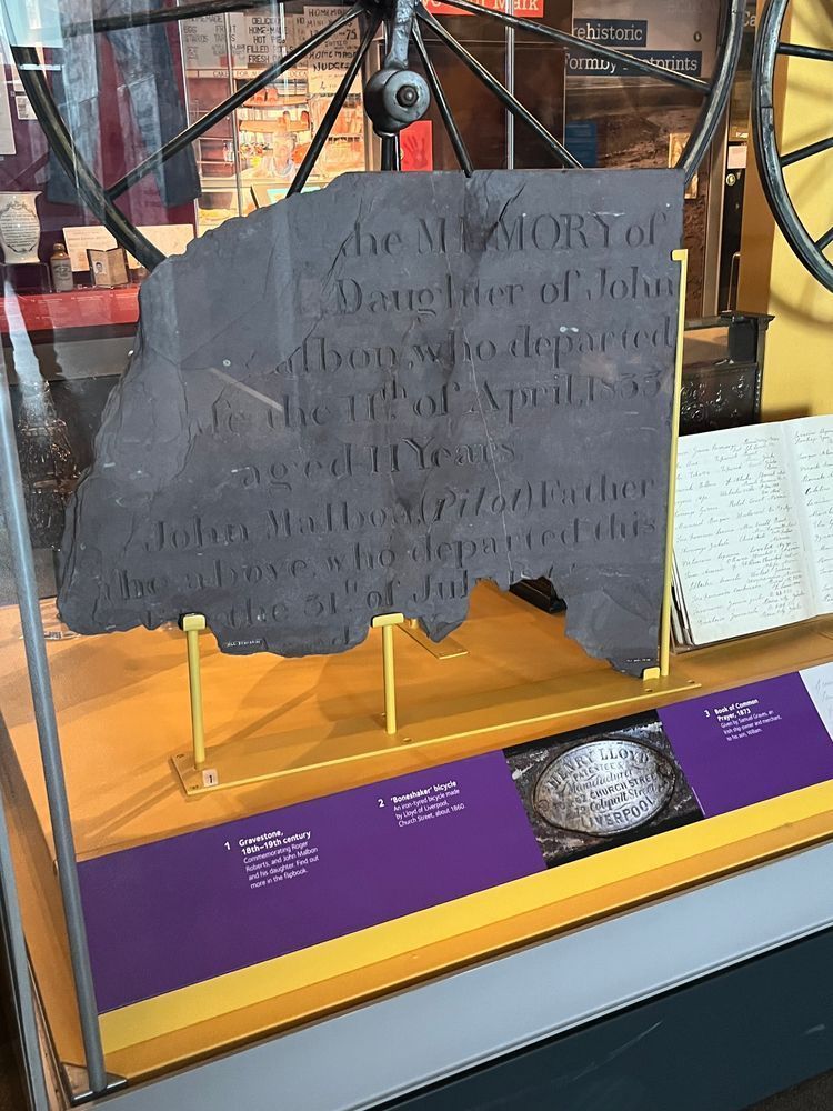 A broken slate gravestone in a display case in a museum. 