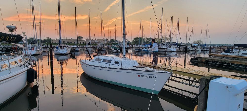 A white sailboat tied up at a dock with the sun setting in the background. 