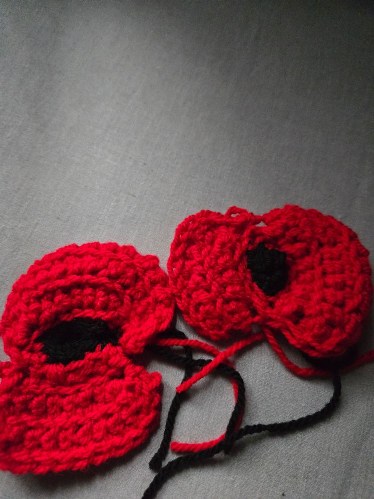 Two red petaled and black centred crocheted poppies. 