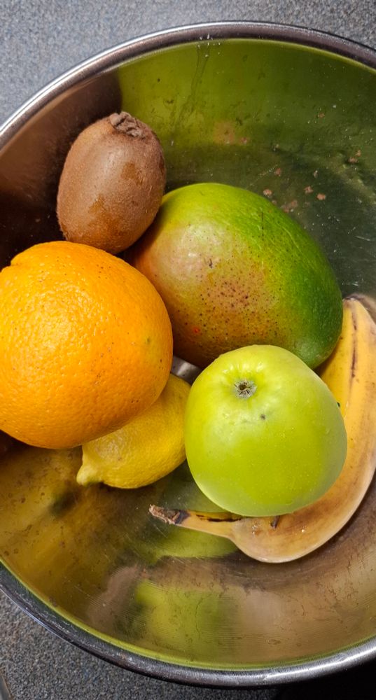 Eine Edelstahlschüssel mit Obst, Mango, Banane, Zitrone, Orange, Kiwi und Apfel im Ganzen