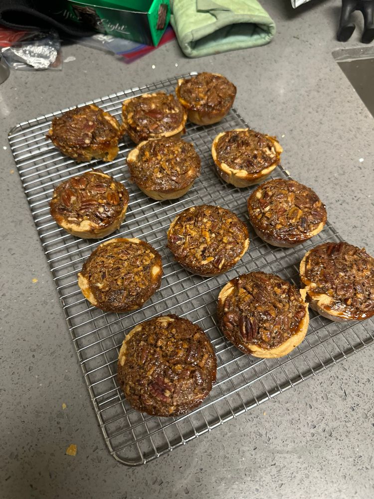 Twelve mini pecan pies cooling on a wire rack