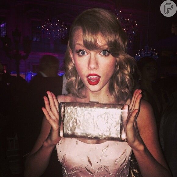 taylor swift at the 2014 met gala in a pink dress holding up a pearlescent pink edie parker clutch