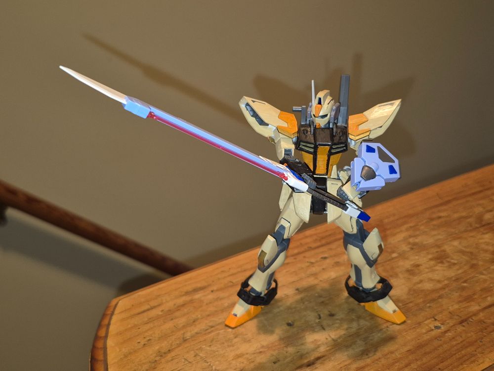 The Baselard grasps it's weapon with both hands, bringing it's point to bear against an unseen enemy target.

The Baselard, like the rest of it's lineage from the Strike Gundam, is designed for versatility, though the improved thrusts and more advanced limbs greatly enhance it's performance in closer ranges. Like this particular example equipped with thr Sword Striker. Like it's rival, the Windam, however, the redesigned shoulder prevent the use of the shoulder equipment modules from the Gen 1 striker paks, but have mo difficulty installing the backpacks. Allegedly, back plugs are compatible with newer generation equipment paks, even from non-Alliance models, but documented evidence of those in use in one of their operations has yet to uncovered.