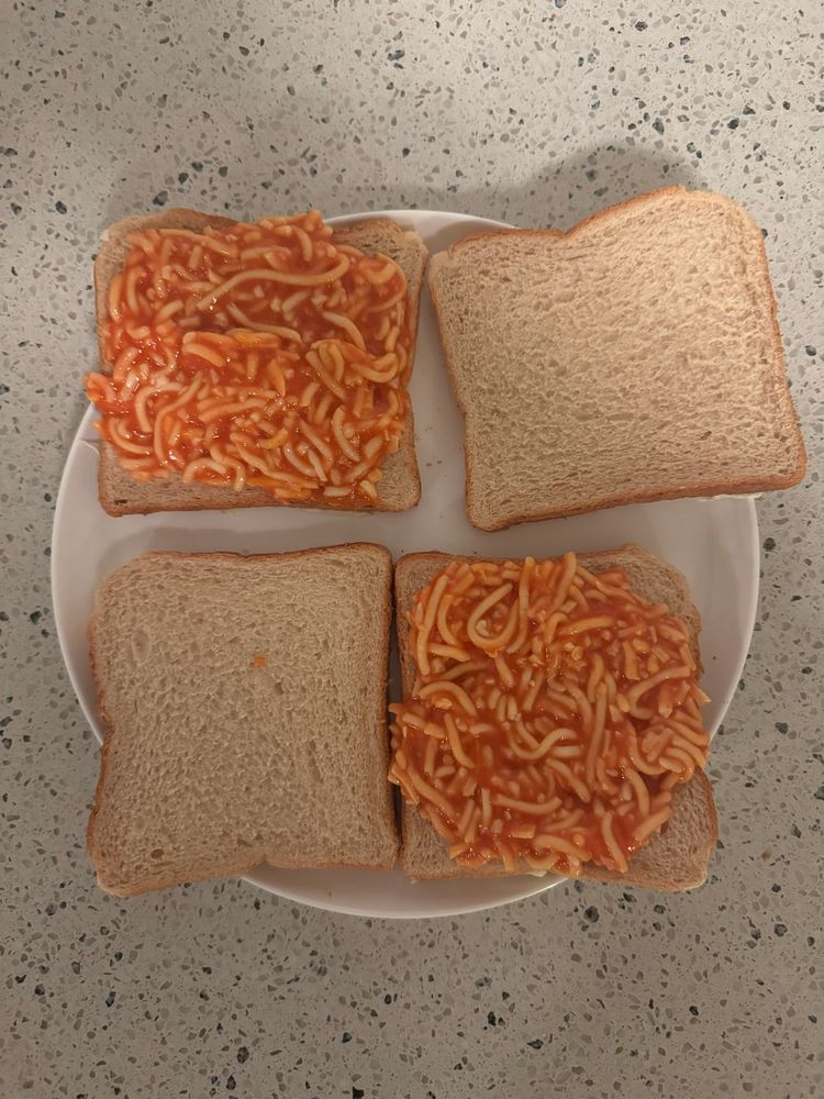 Photo of the spaghetti mix on two of the 4 pieces of bread, on a plate on a bench top. 