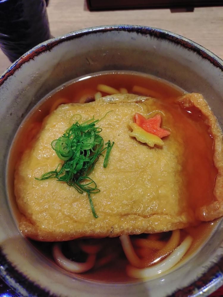 大きな油揚げと刻みネギともみじの形の麩がのったうどん