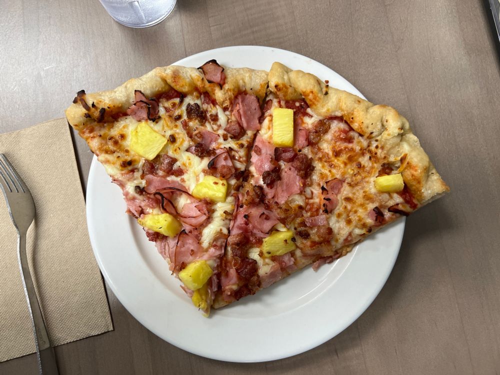 Two slices of pineapple, ham, and bacon pizza on a plate.