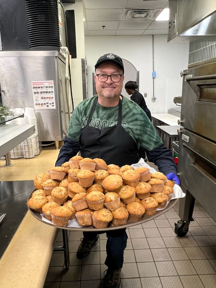 A middle aged man holds a plate of muffins.