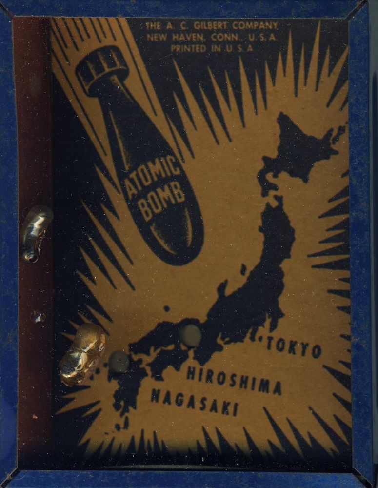 Photo of a metal toy box with a plastic cover, inside is a graphic showing an atomic bomb above a map of Japan. 