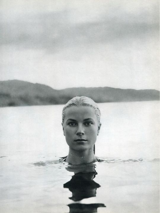 📷 Howell Conant 
A black & white photograph of Grace Kelly up to her neck in the sea, looking directly into the camera, with her reflection in the water rippling towards it. In the background we can see a strip of land and then the sky with a streak of grey In the clouds. I have added the photograph to a past thread of similar photographs. This is the fourth in the sequence.
