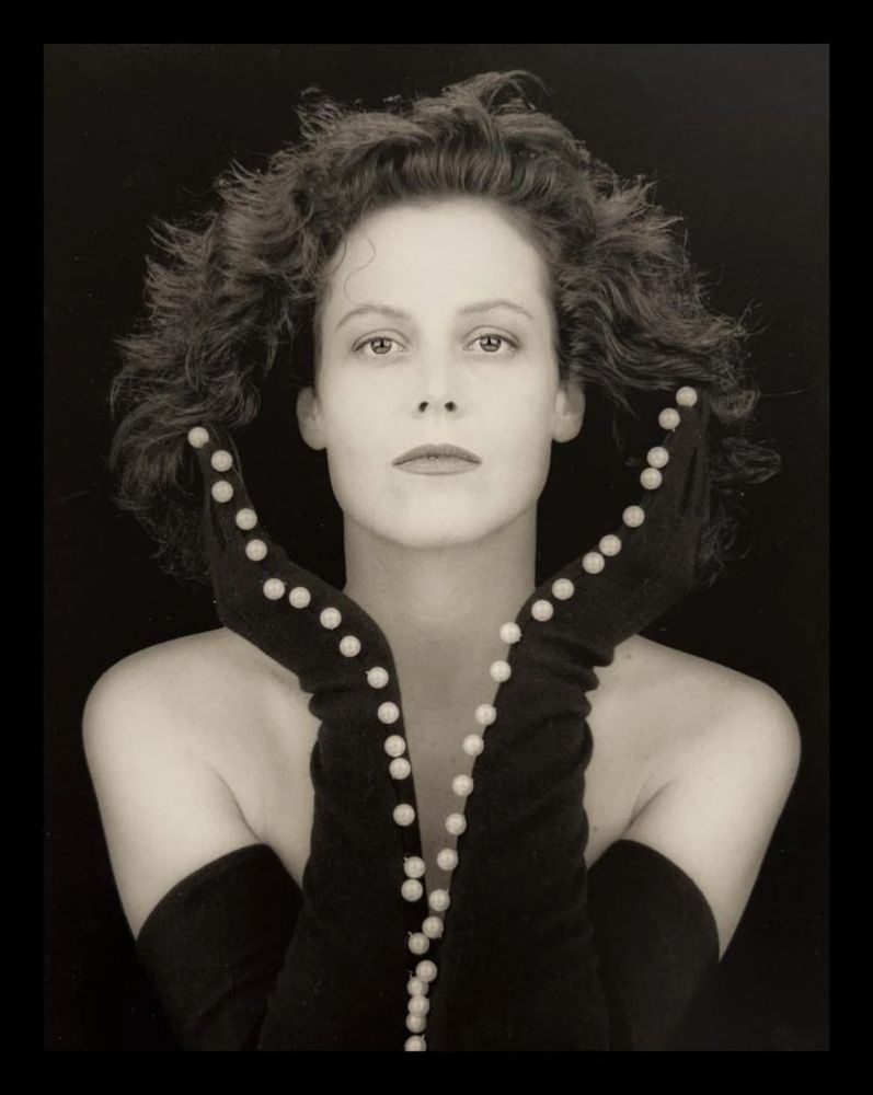 📷 Robert Mapplethorpe 
Black & white photograph of Sigourney Weaver. Background dark grey at top descends to black. Weaver, bare shouldered, black long gloves to her armpit almost, elbows together then arms split towards hands seen in profile forming a vase-like shape around the bottom half of her face accentuated by a line of pearls from the tip of the little finger to the elbow on each glove. Her hair brushed outwards beyond the vase of her hands. She could have been perfectly symmetrical but the meeting of her elbows is just off centre to the left, deliberate. At the bottom the black of her elbows and the background match. For the purposes of this thread she is a plant.