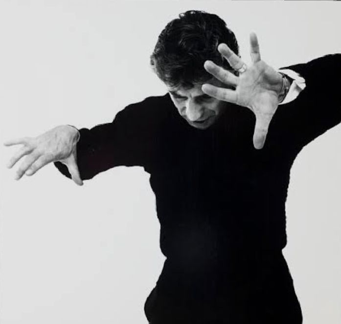 📷 Richard Avedon 
Black & white photograph of Leonard Bernstein in a conductor's pose, head down hands up, fingers spread, black clothing, just a white cuff can be seen, black hair, all white background. He might be parting curtains or separating two fighting school children.