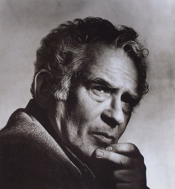 📷 Irving Penn 
Black & white photograph of Norman Mailer. He is side-on, but his head is turned towards us slightly with his eyes looking past the picture plane to our right - if the edge of the photograph were the frame of a window then he is looking out of the window but ignoring us to our right. He has two fingers from his left hand on the middle of his chin, his thumb which we can't see will be against his jaw, the bottom of the photograph crops his little finger slightly so we don't see his full hand. It is a recognisable thinking, examining, contemplating, judging pose - it's an act, a photograph for the back of a book, the writer. The background, plain, lit, dusty charcoal like patches. The play of shadows on his face where we see shadows either side, lit from somewhere above and Infront, could even be a window it has an almost natural feel.