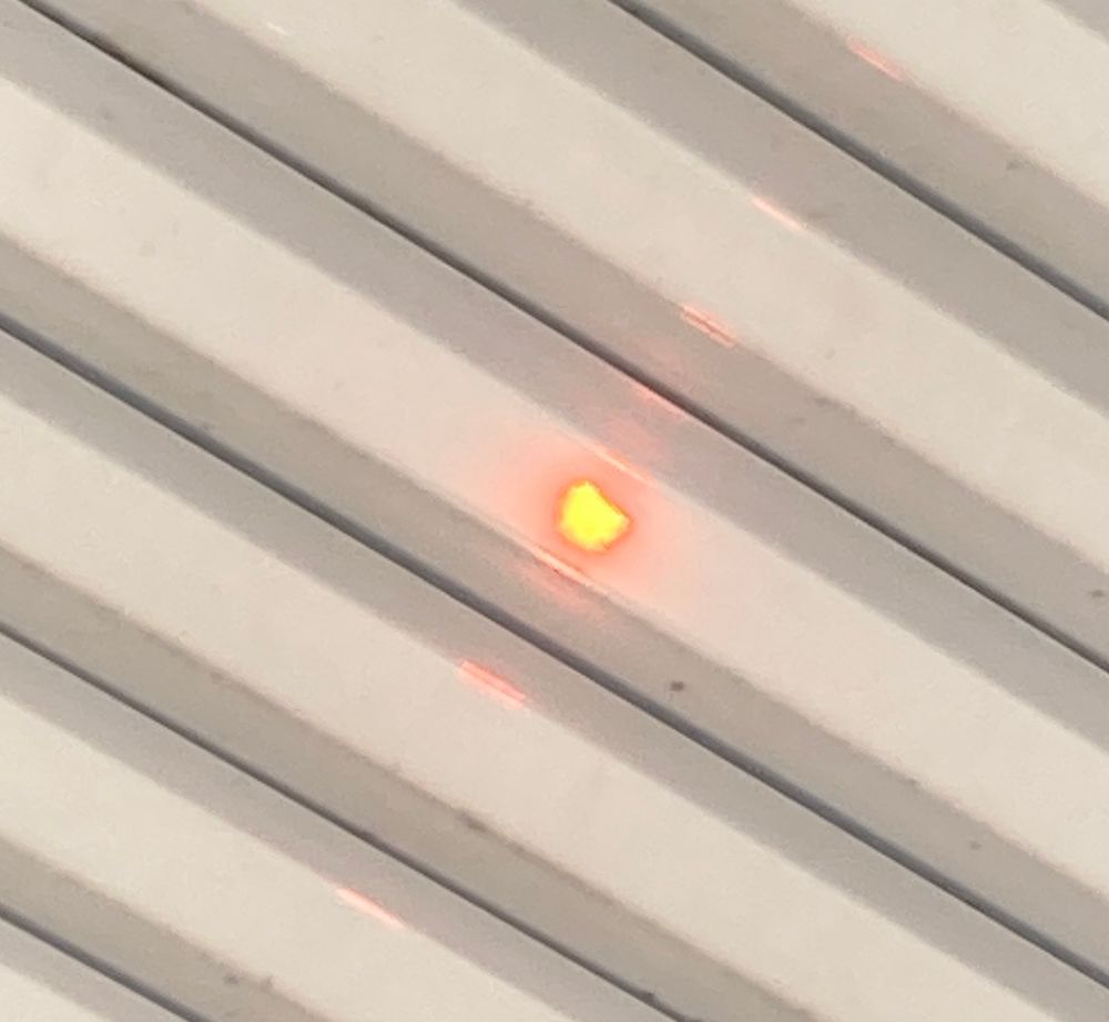 A partial solar eclipse seen through white semi transparent plastic. The sun disc is a bit blurry, but the moon’s shadow is clearly visible. 