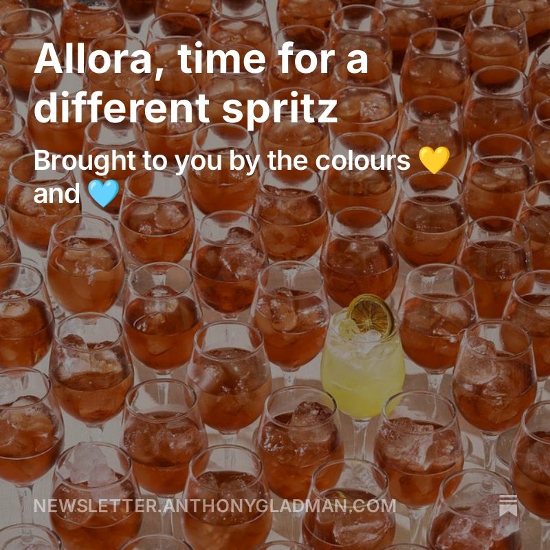 There are lots of glasses in this picture. They all contain an iced drink. They are all orange apart from one, which is bright yellow and the only one to have a garnish (a dried lemon wheel). There is text overlaid which reads: "Allora, time for a different spritz" and "brought to you by the colours 💛 and 🩵".