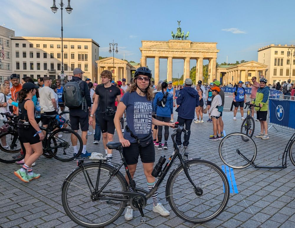Ich stehe ein Stück entfernt vor dem Brandenburger Tor, und halte mein Rad vor mir fest. Im Hintergrund sind weitere Menschen.