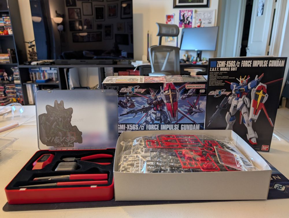 Open plastic model hobby kit to the left and an opened box for the Force Impulse Gundam plastic model kit to the right. Plastic runners are exposed in the open box and the front page for the build manual is a bit further to the right