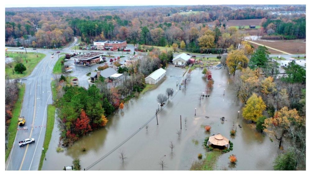 An aerial photo of a town with flooded streets and buildings surrounded by roads and trees