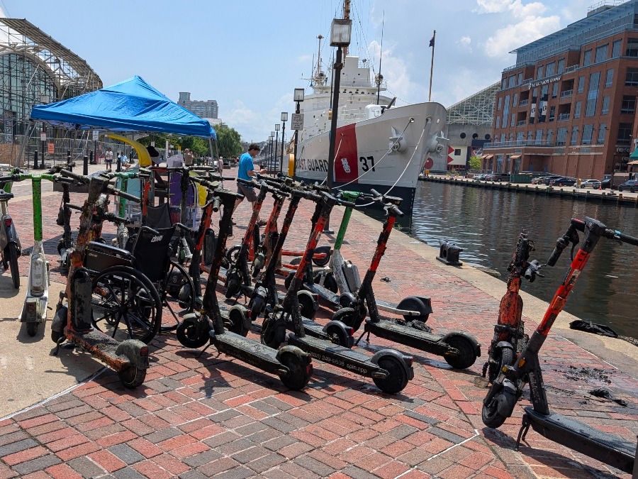 Muddy motorized scooters and a wheel chair pulled from the water and placed on a brick walkway of a pier in Baltimore's Inner Harbor