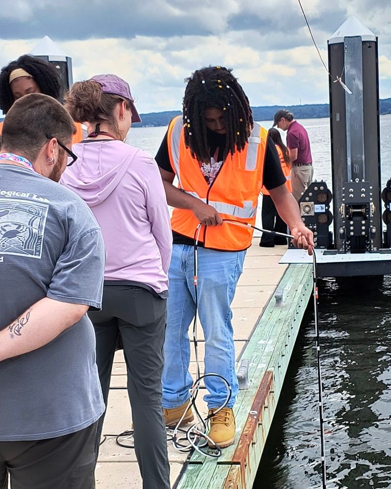 Students on a pier watch as one student lifts a line out of the water