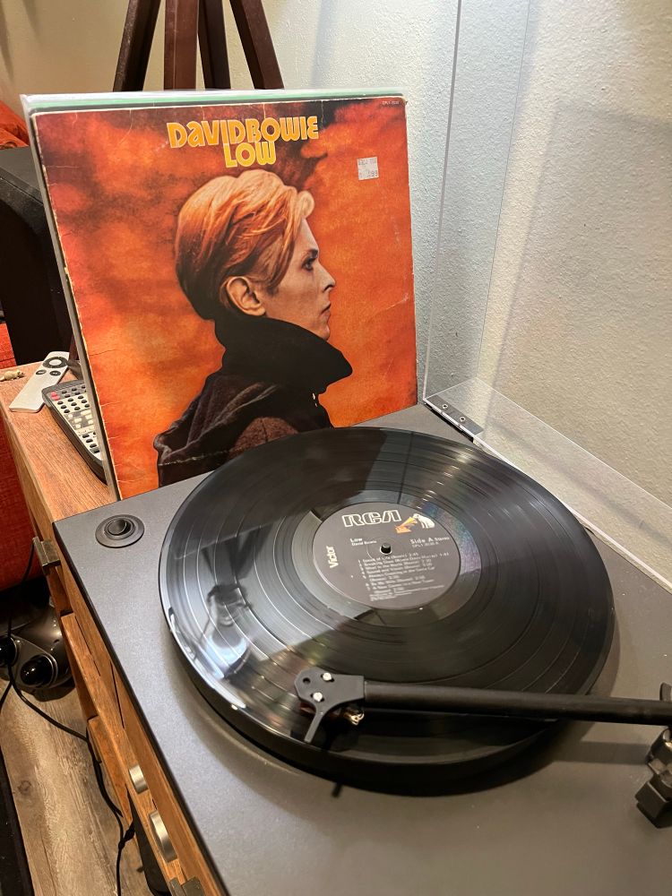 A turntable with a record playing; David Bowie’s Low LP jacket is leaning alongside