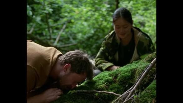 a man squinting to look at moss with a woman in the background