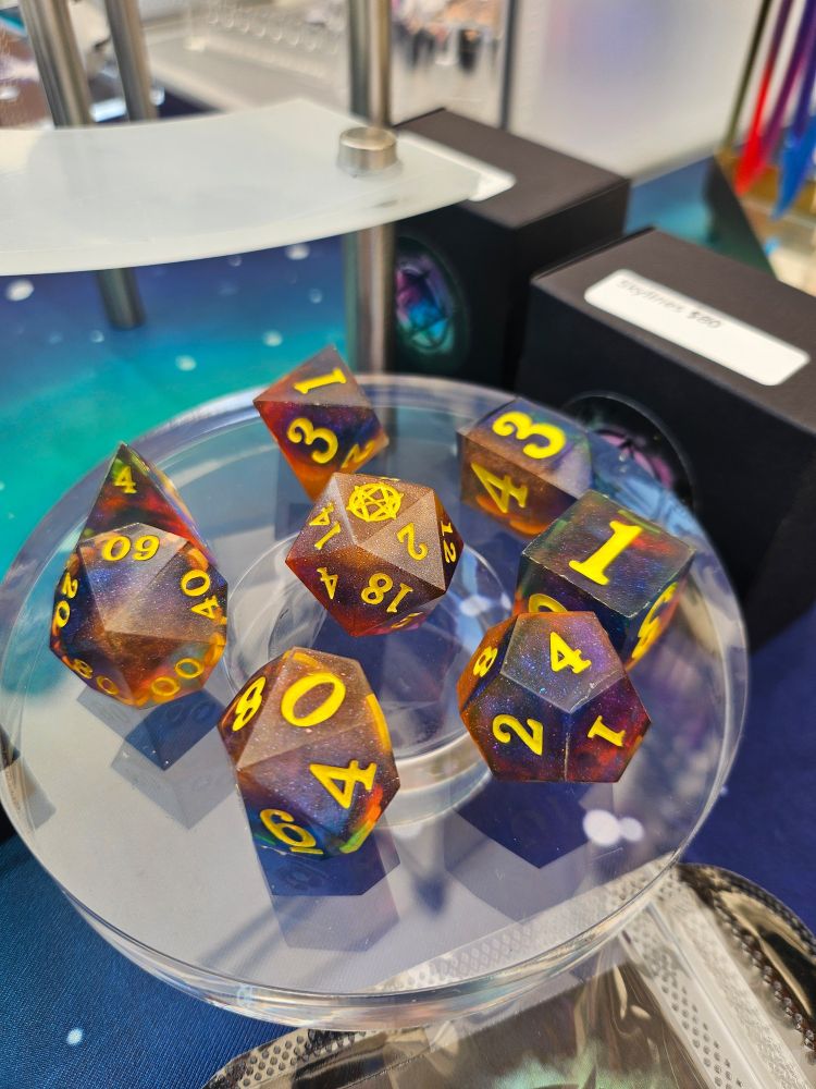 A set of polyhedral dice in rich navy, orange, and yellow colors with glitter and bright yellow numbers, named Skylines
