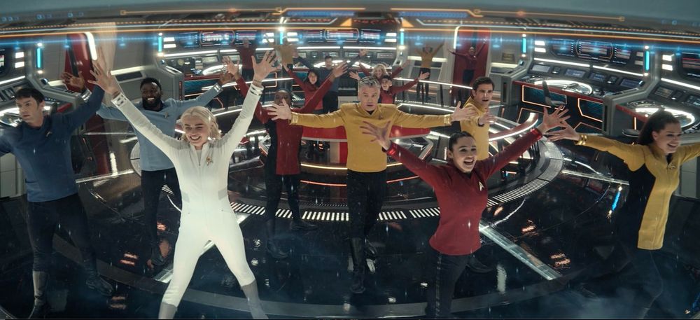 the crew of the starship Enterprise (Strange New Worlds era) reach joyfully to the sky, having just completed a successful mission and a musical number. They are all smiling widely except Spock, who is Vulcan, and Pike, who is no fun. 