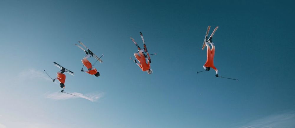 Ein Skifahrer von Swiss-Ski bei einem akrobatischen Sprung in der Luft, der Himmel im Hintergrund ist blau.