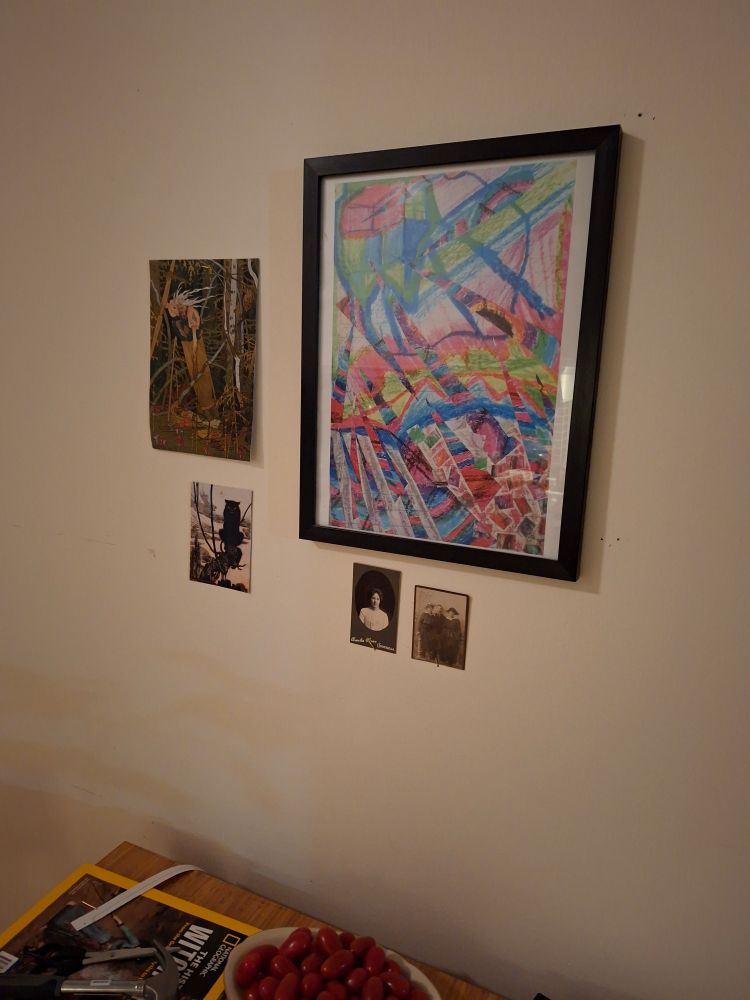 An abstract colorful painting on a white wall. To the left two cut out pictures of baba jaga and a witch cat. Underneath two small potraits from early 1900.