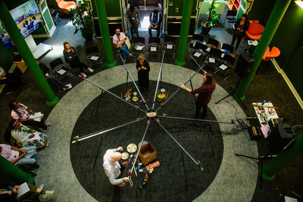 An 8 metre wide, 8 legged stringed instrument being played in a circular room, seen from above.