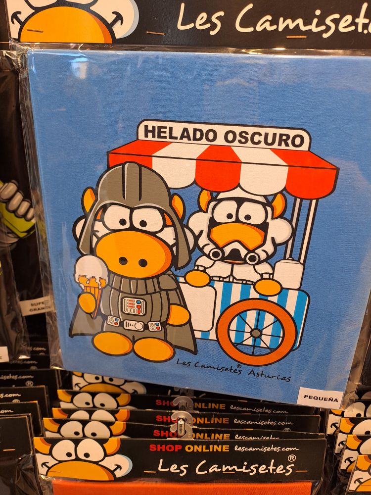 Camiseta con estampado de dos vacas, ambas vestidas de las guerras d ella galaxias, uno de blanco bajo una caseta de venta de helados y uno de negro co un helado en la mano y arriba un cartelito que reza: "Helado oscuro"