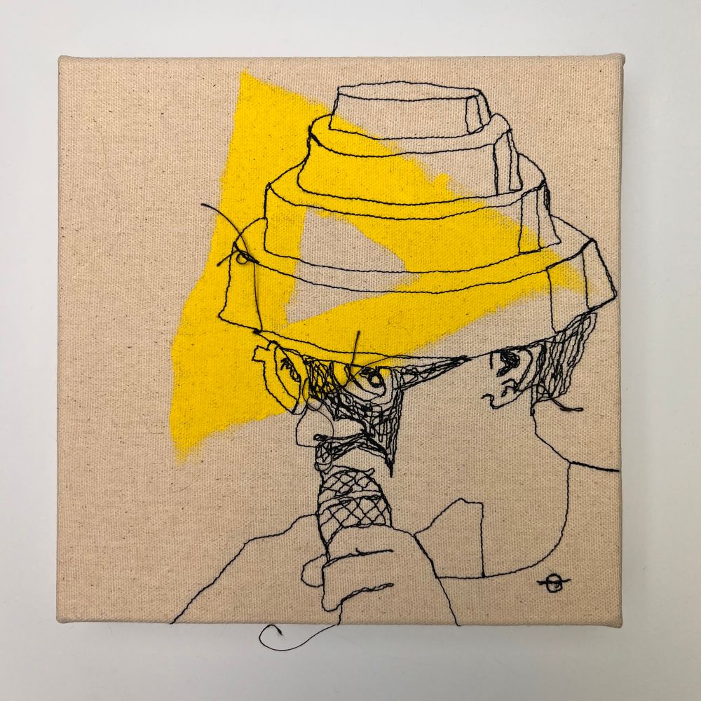 Black thread portrait of man in glasses holding a microphone and wearing a pyramid hat. The portrait is stitched onto canvas, painted with a yellow triangle.