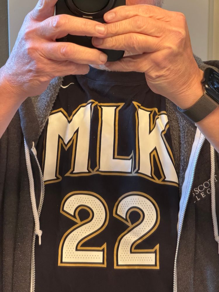 Tom is modeling a shirt in the style of the Atlanta Hawks’ first City uniforms, with an MLK logo in white on black with gold outlines. 