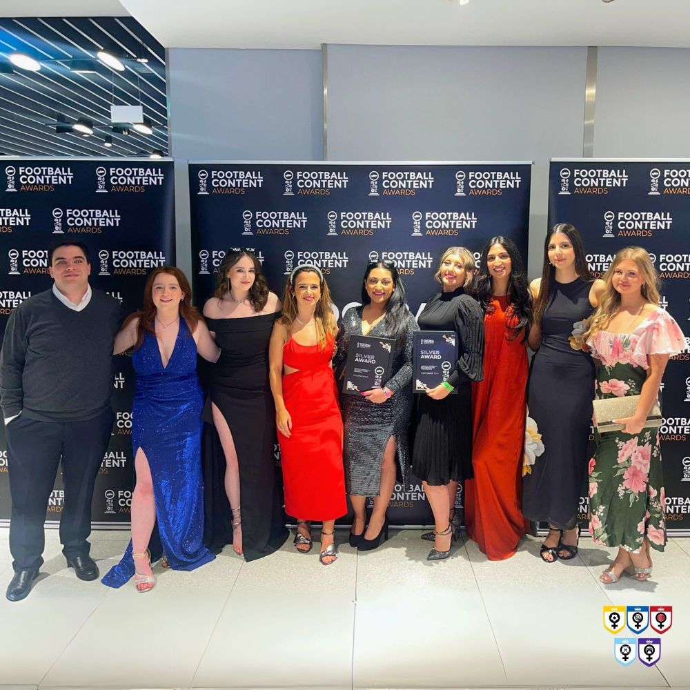 From left to right: Finley, Aimee, Chloe, Eve, Roopa (me), Caz, Priyanka, Simran and Liv from Her Game Too dressed to the nines stood in front of branded Football Content Awards boards with our 2 silver awards.