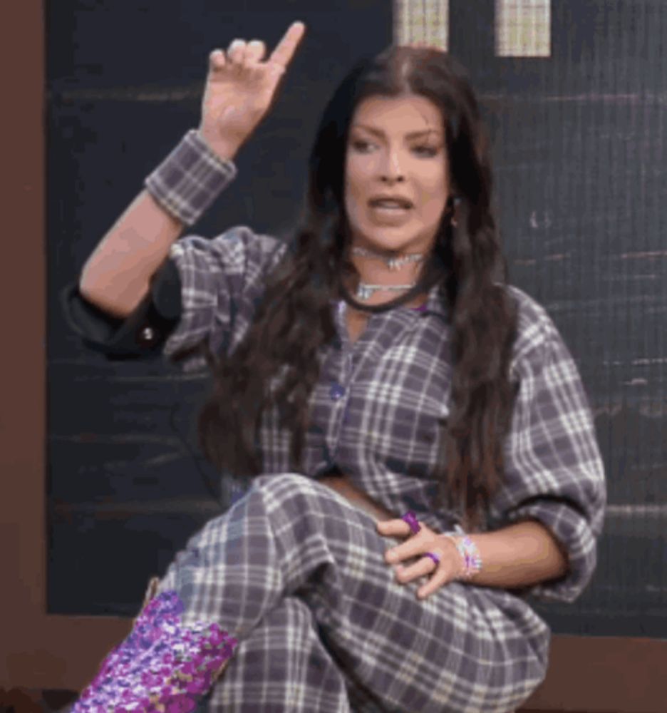 a woman in a plaid shirt and purple boots is sitting down and making a gesture with her hand .