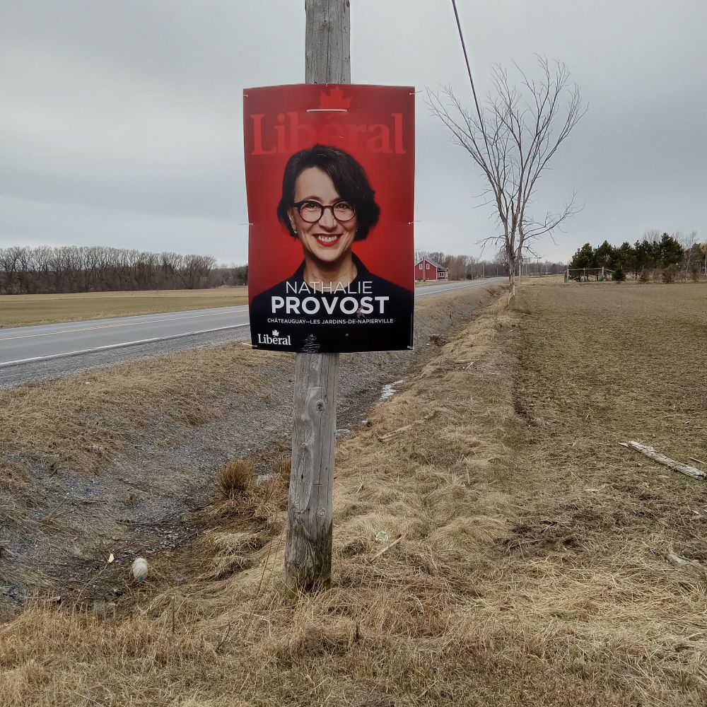 A Liberal party election sign for Nathalie Provost attached to hydro pole on the edge of a field.