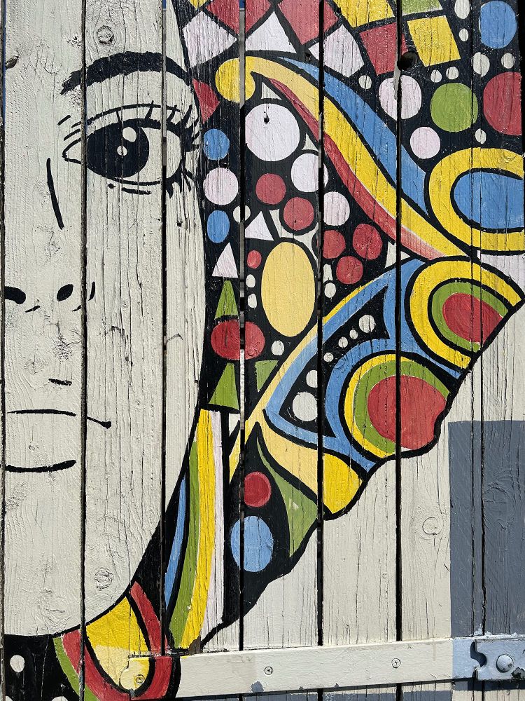 A cropped close-up of the art from the pervious image featuring the left side of the subject's face and colourful circles, diamonds, triangles, and swirls. Hosier Street, Reading, Berkshire, UK. Photo by Gearóid Burke. 