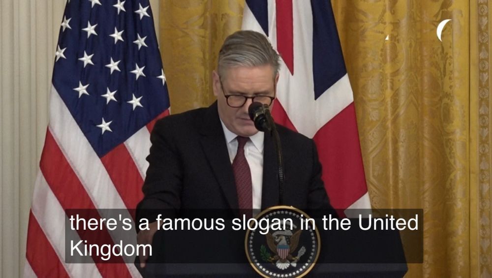 U.K. Prime Minister Keir Starmer standing in front of the flags of the U.K. and U.S.A. Captioned with the phrase ‘there’s a famous slogan in the United Kingdom’.
