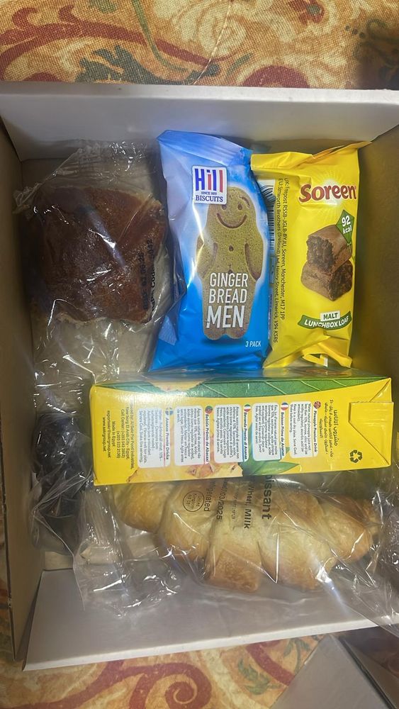 a box with croissant, cake, ginger bread man and soreen bread.
