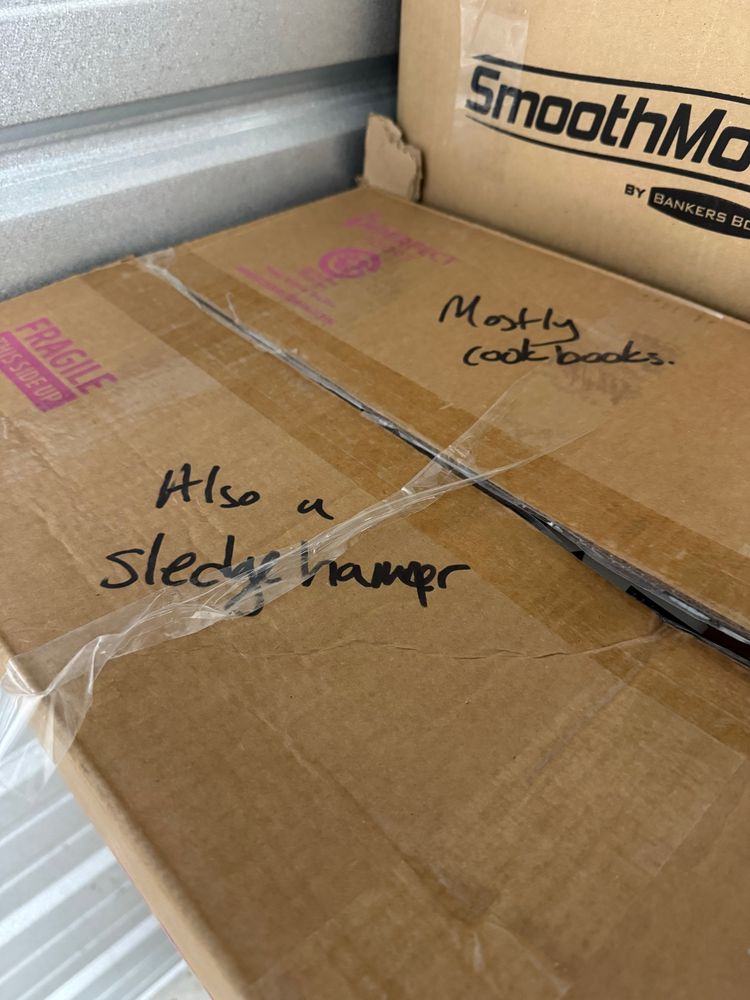 A cardboard box labeled “Mostly cookbooks; Also a sledgehammer”