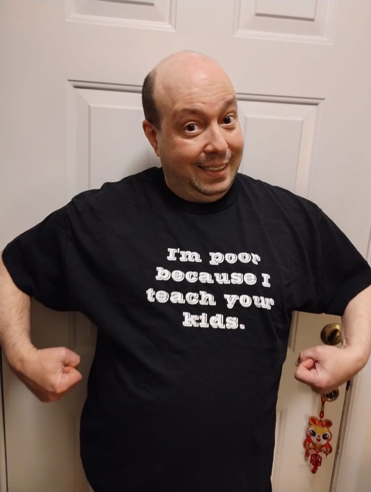 A picture of me with a goofy expression on my face. I'm wearing a black tee shirt with a caption in white letters that reads, "I'm poor because I teach your kids."
